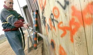 Councilman Bob Weiner cleans graffiti from a sample wooden fence with the Farrow System, which uses water and pulverized rock to remove paint without damage to the surface. A West Chester, Pa., company donated the $16,000 machine to the Citizens Anti-Graffiti Brigade, a volunteer group.